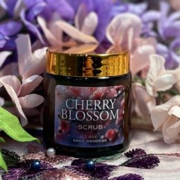 Cherry Blossom Scrub jar with gold lid on floral cloth with pink and purple flowers in the background