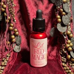 Lil Red Magic serum in red bottle, black dropper on a red velvet cloth with coins & bead tassels background