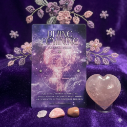 Divine Feminine Crystal Quad card displayed on a deep purple velvet cloth with delicate beaded pink and lavender flowers in the background, three small tumbled stones lined up in front, and a large polished rose quartz heart on a stand to the right.