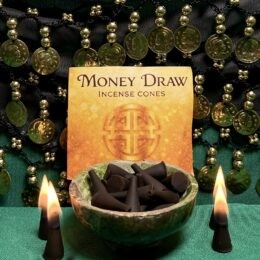 Alt text: “Money Draw incense cones displayed in a green stone bowl in front of a golden ‘Money Draw Incense Cones’ label, with four burning black cones and a backdrop of green fabric and hanging gold coins.”