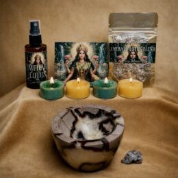 An Emerald Lotus New Moon in Taurus ritual set is arranged on gold fabric, featuring a brown and yellow stone offering bowl, four lit green and gold tealights, an herbal blend pouch, a mist bottle, and a goddess image card.