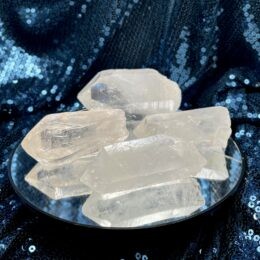 Several large, clear quartz points rest on a round mirrored surface, reflecting their icy white glow against a dark blue sequined fabric background.