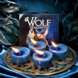 Four lit blue tealight candles sit on a golden tray in front of a “Wolf Tealights” box with a mystical wolf and woman under a starry night sky.