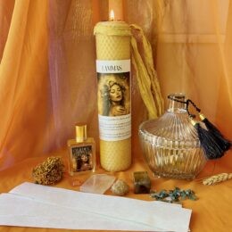 Lammas ritual set with a tall honeycomb beeswax candle, glass perfume bottle, Golden Harvest perfume, crystals, herbs, and wheat arranged on an orange cloth backdrop.